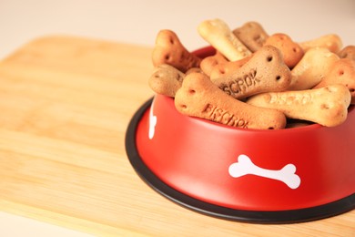 Photo of Bone shaped dog cookies in feeding bowl on wooden table, closeup. Space for text