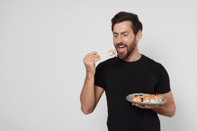 Happy man eating tasty sushi roll with chopsticks on light grey background. Space for text