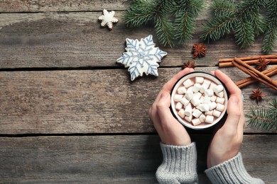 Woman holding cup of delicious hot chocolate with marshmallows at wooden table, top view. Space for text