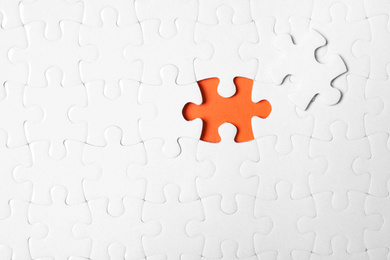 Blank white puzzle with separated piece on orange background, top view