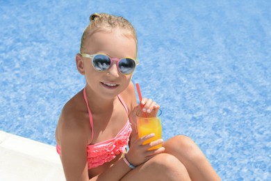 Cute little girl with glass of juice at swimming pool edge on sunny day