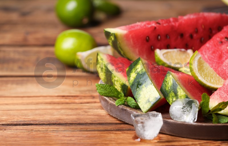 Slices of delicious ripe watermelon, ice cubes and cut lime on wooden table, closeup. Space for text