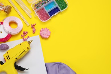 Hot glue gun and handicraft materials on yellow background, flat lay. Space for text