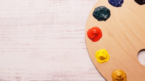 Photo of Artist's palette with samples of colorful paints on white wooden table, top view. Space for text