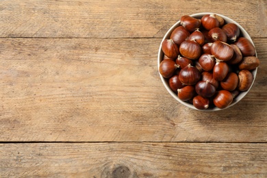 Fresh sweet edible chestnuts in bowl on wooden table, top view. Space for text