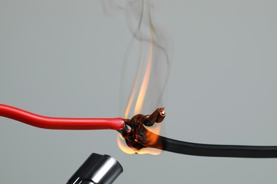 Photo of Inflamed red wire on grey background, closeup. Electrical short circuit