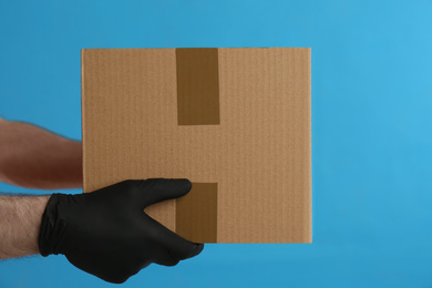 Courier holding cardboard box on blue background, closeup. Parcel delivery