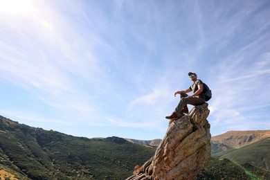 Man with backpack on rocky peak in mountains. Space for text