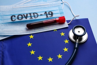 European Union flag, protective masks and test tube with blood sample on light blue background. Coronavirus outbreak