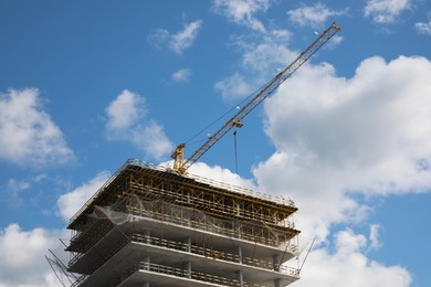 Photo of Construction site with tower crane on unfinished building under blue cloudy sky