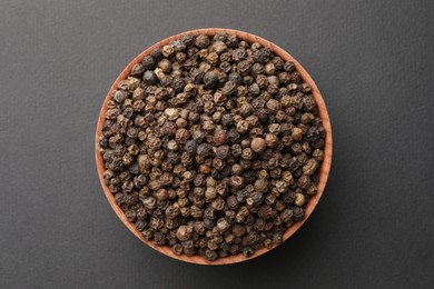 Photo of Bowl of spicy black pepper grains on grey background, top view