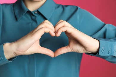 Photo of Woman making heart with her hands on pink background, closeup