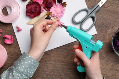 Photo of Woman using hot glue gun to make craft at wooden table, top view