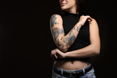 Beautiful woman with tattoos on arm against black background, closeup. Space for text