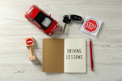 Flat lay composition with workbook for driving lessons and road signs on white wooden background. Passing license exam