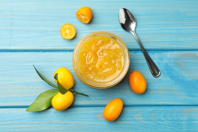 Jar of delicious kumquat jam, spoon and fresh fruits on light blue wooden table, flat lay