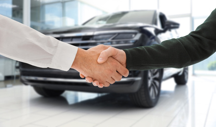 Image of Man buying car and shaking hands with salesman against blurred auto, closeup