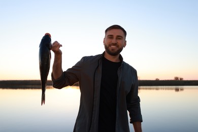 Photo of Fisherman holding caught fish at riverside. Recreational activity