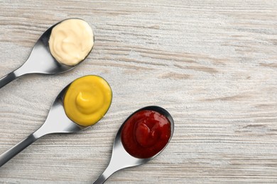 Spoons with mustard, ketchup and mayonnaise on wooden table, flat lay. Space for text