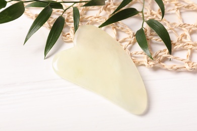 Photo of Jade gua sha tool and branches on white wooden table, closeup