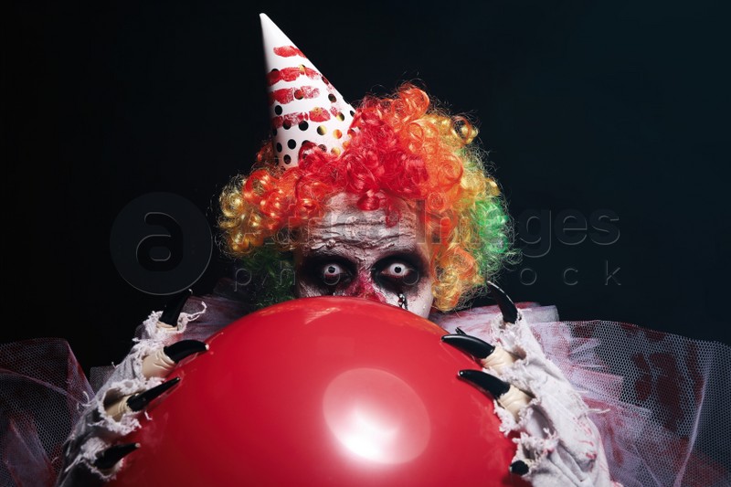 Terrifying clown with red air balloon on black background. Halloween party costume