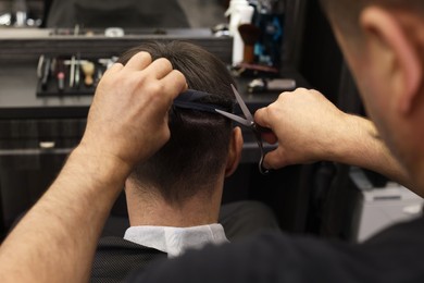 Professional hairdresser cutting man's hair in barbershop