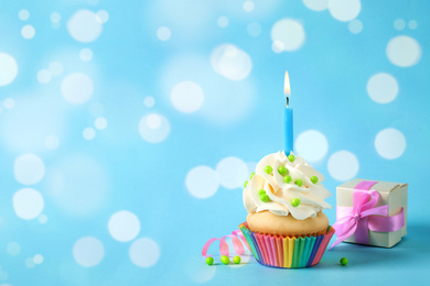 Birthday cupcake with candle and gift box on light blue background, space for text. Bokeh effect