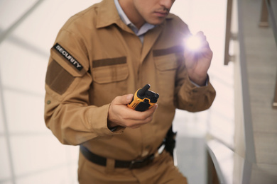 Professional security guard with portable radio set and flashlight indoors, closeup