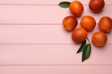 Many ripe sicilian oranges and leaves on pink wooden table, flat lay. Space for text