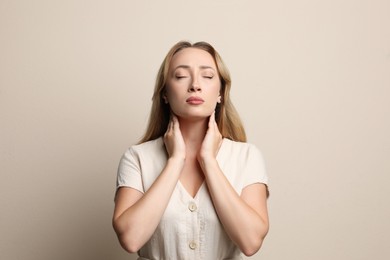 Young woman doing thyroid self examination on beige background