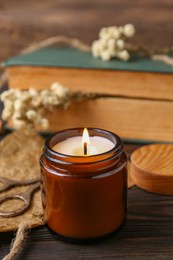 Photo of Burning scented candle, book and flowers on wooden table