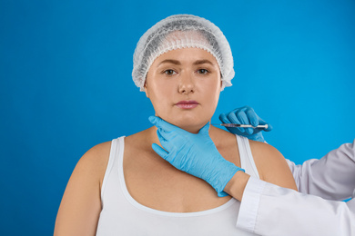 Woman with double chin getting injection on blue background. Cosmetic surgery