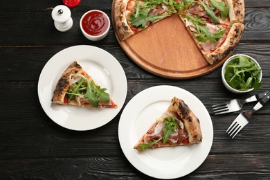 Photo of Tasty pizza with meat and arugula on black wooden table, flat lay
