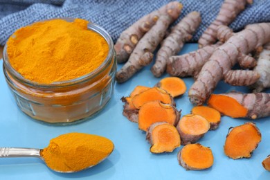 Photo of Glass jar of turmeric powder and roots on light blue tray
