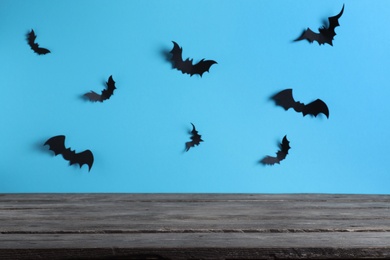 Empty wooden table near light blue wall decorated with paper bats. Halloween celebration