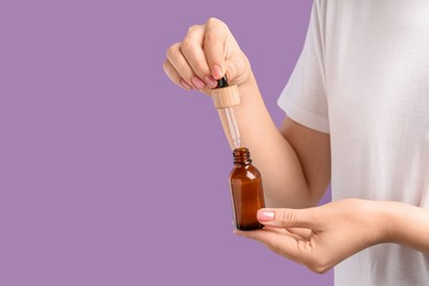 Woman dripping serum from pipette into bottle against lilac background, closeup. Space for text