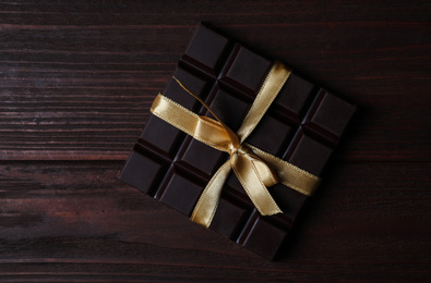 Tasty dark chocolate bar with ribbon on wooden table, top view