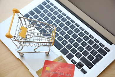 Internet shopping. Small cart and credit cards on laptop, closeup