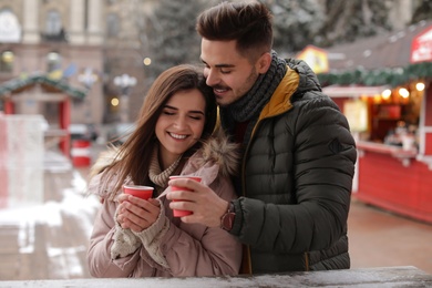 Young couple with cups of mulled wine at winter fair