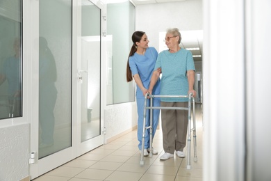Nurse assisting senior patient with walker in hospital hallway