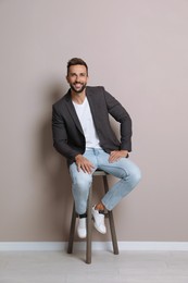 Handsome man sitting on stool near beige wall