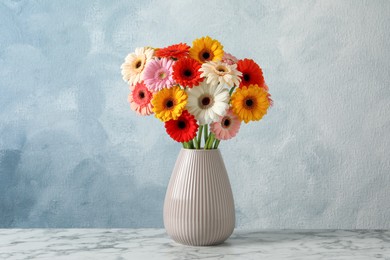 Photo of Bouquet of beautiful colorful gerbera flowers in vase on white marble table against light blue background