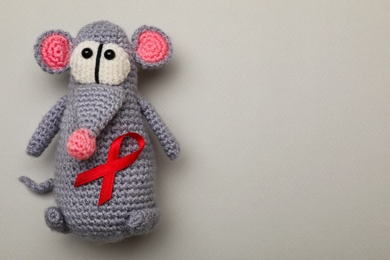 Cute knitted toy mouse with red ribbon on beige background, top view and space for text. AIDS disease awareness