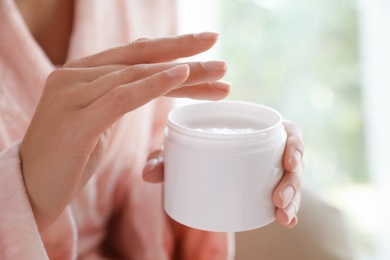 Woman with jar of moisturizing cream on blurred background, closeup