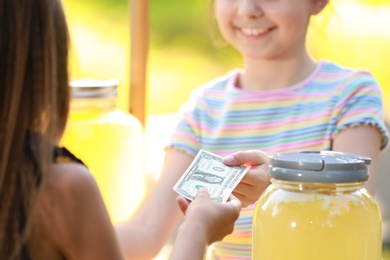 Little girl selling natural lemonade to kid in park, closeup. Summer refreshing drink