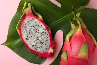 Delicious cut and whole white pitahaya fruits with green leaf on light pink background, flat lay