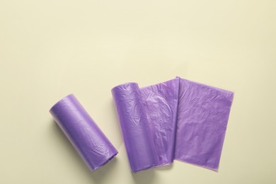 Photo of Rolls of purple garbage bags on beige background, flat lay. Space for text