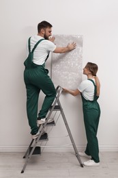 Workers hanging stylish wall paper sheet indoors