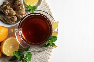 Cup of delicious ginger tea, mint leaves and lemons on white wooden table, top view. Space for text