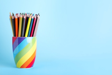 Colorful pencils in cup on light blue background. Space for text